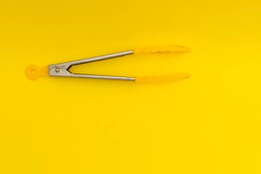 Yellow pasta tongs on yellow background, monochrome