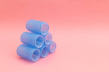 Large blue hair curlers on a bright pink background