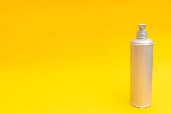 Sarı arka planda gri şampuan şişesi.