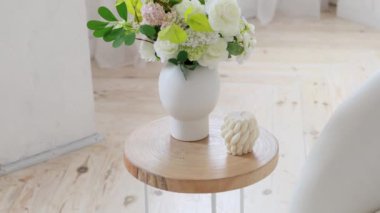 Masanın üzerinde bir mum ve çiçekler var, büyük parlak bir odada.