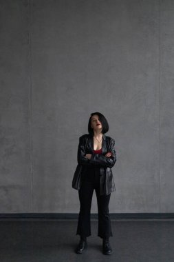 Kırmızı bluzlu ve deri ceketli bir kız karanlık bir duvara yaslanmış, dikey bir fotoğraf.