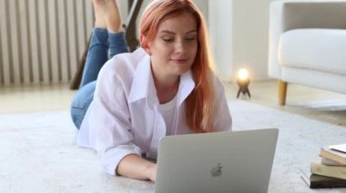 Kızıl saçlı bir kız dizüstü bilgisayarla yerde yatıyor.