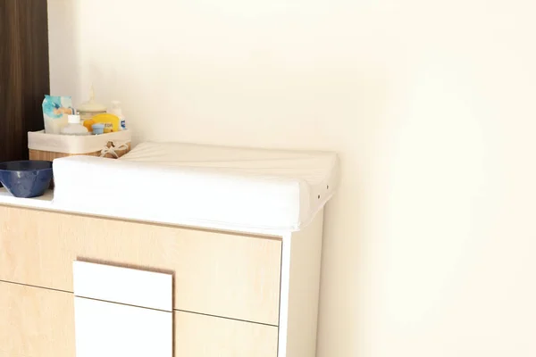 Small changing table and beidge chest of drawers. Concept of organizing baby care things in a small space. Copy space.