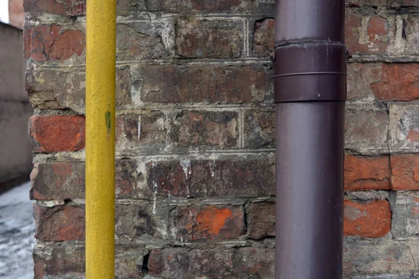 An old red shabby wall with a large plastic purple pipe and a thin yellow pipe.