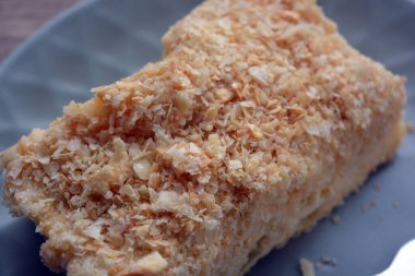 A delicious, well-fed tender piece of light and airy Napoleon cake is located on a gray-blue plate with a fork.