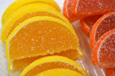 Yellow and orange jelly sweets made in the form of sliced orange slices, lemon, fruits located in plastic transparent containers and sprinkled with sugar.