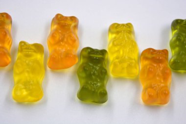 Bright children's orange, green, yellow chewing, jelly candies in the form and in the form of colored bears are located on a white background.