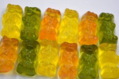 Bright children's orange, green, yellow chewing, jelly candies in the form and in the form of colored bears are located on a white background.