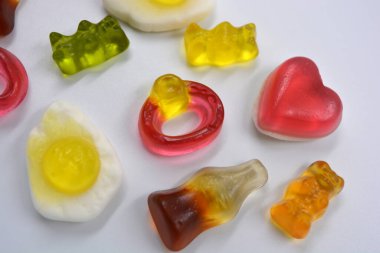 Beautiful and bright children's chewing, jelly sweets of different shapes, in the form of fried scrambled eggs, a bottle of cola, colored bears, rings with stones, a pink heart are located chaotically on a white background.