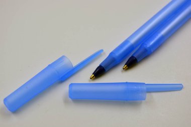 Bright and beautiful two pens with blue ink and two caps made of blue plastic are located on a white background.