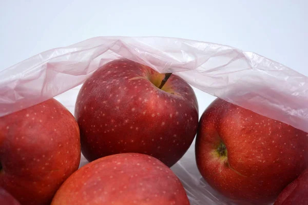 A large package of fruit, healthy food, a lot of red, ripe apples lie in a pink disposable bag.