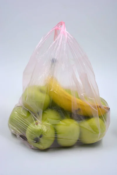 A large package of fruit, healthy food, many green simerenko apples and one ripe banana lie in a pink disposable bag.