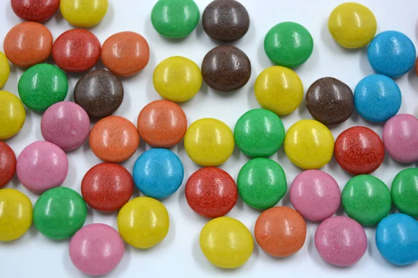 Bright and colorful, multi-colored chocolate candies covered with red, blue, yellow, green, pink, orange, chocolate coating are located chaotically on a white background.