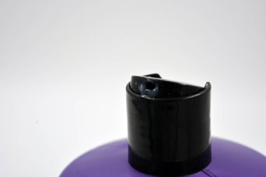 Beyaz arka planda siyah kapaklı büyük, mor bir plastik şampuan şişesi..
