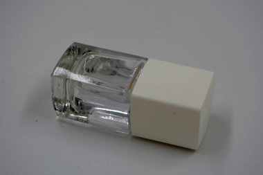 Beyaz kapaklı bir ahududu cam şişesinde kadın tırnağı cilası ve beyaz arka planda siyah bir fırça bulunur..