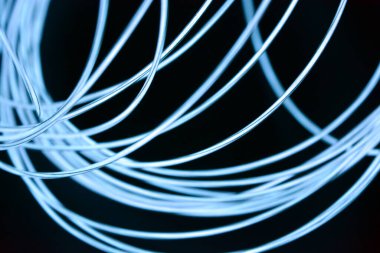 İnce ışık kablolarından oluşan parlayan bir kaos. Alışılmadık, eşsiz, kaotik bir şekilde parlayan ince kablolar, gök mavisi, açık mavi, neon kayış takımı, aydınlatma kablosu, ince bir arkaplana yerleştirilmiş ince kablo..