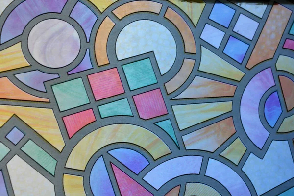 Unusual hand-drawn color film with a mosaic pattern glued to the glass of the balcony of an apartment. Graphic squares, circles, circles, and angles.