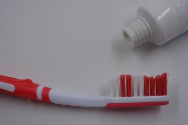 Kişisel hijyen ürünleri, kırmızı ve beyaz tüylü yeni bir plastik diş fırçası, beyaz plastik arka planda kırmızı kauçuk ve diş macunu.. 