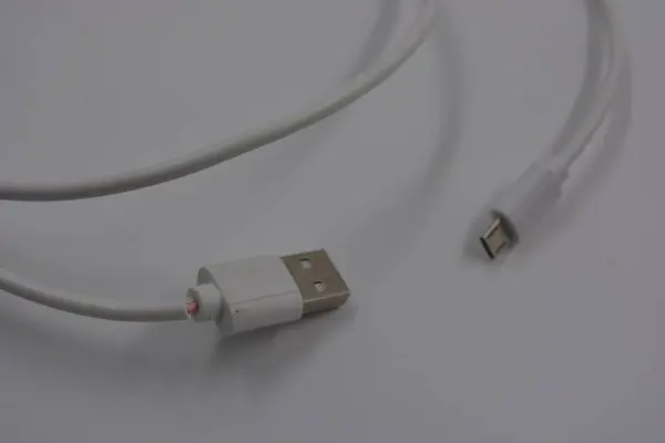 Computer quipment long, white micro USB cable for phone, computer located on white plastic background.