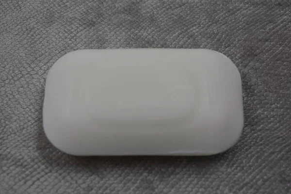 Beautiful, stylish, white bar of soap without logo and name placed on a gray, scaly velvet background.