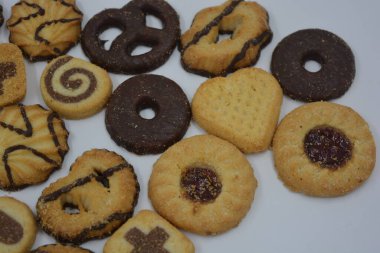 Çikolata ve reçelle kaplı, farklı şekillerde ve tiplerde güzel, parlak bir kurabiye çeşidi. Beyaz çalışma arka planına yerleştirilmiş fırınlanmış mallar.