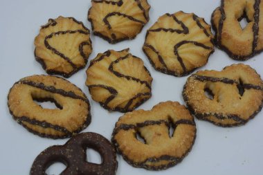 Çikolata ve reçelle kaplı, farklı şekillerde ve tiplerde güzel, parlak bir kurabiye çeşidi. Beyaz çalışma arka planına yerleştirilmiş fırınlanmış mallar.