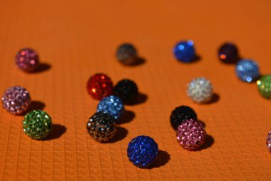 Güzel, parlak, çok renkli toplar Swarovski kristalleri kaotik bir şekilde parlak turuncu arka planda dizilmiş..