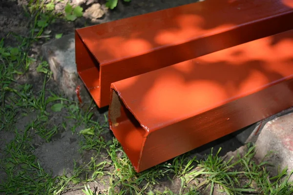 İnşaat malzemeleri, inşaat ve onarım malzemeleri. Uzun, kalın, metalik profil taze kahverengi boyayla kaplı. Özel bir arsada profil oluşturuluyor.