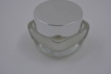 Kadın kozmetik ürünleri, aksesuarlar, nemlendirme için beyaz krem, bakım, gümüş kapaklı güzel cam bir kavanozda yüz bakımı ve beyaz plastik bir arka plan..