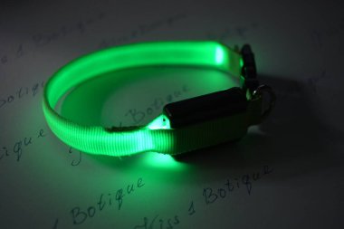 Evcil hayvan aksesuarları, kedi ve köpekler için parlayan bir tasma, yeşil parlayan ve beyaz bir kağıt parçasının üzerinde yer alan.