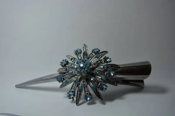 Beautiful women\'s jewelry, steel and elegant costume jewelry. Grey metal hair clip with large metal flower made of blue stones set on white background.