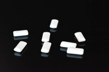 Yiyecek, kişisel bakım ürünleri, ürün, sakız, beyaz çiğneme yastıkları, siyah parlak bir arka planda sıralanmış sakız..