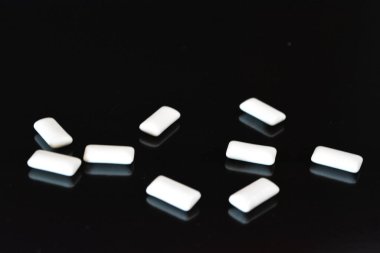 Yiyecek, kişisel bakım ürünleri, ürün, sakız, beyaz çiğneme yastıkları, siyah parlak bir arka planda sıralanmış sakız..