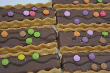 Tatlılar, lezzetli, ilginç tatlılar, karamelli kurabiyeler, sütlü çikolata ve beyaz arka planda küçük renkli şekerler..