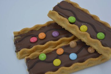 Tatlılar, lezzetli, ilginç tatlılar, karamelli kurabiyeler, sütlü çikolata ve beyaz arka planda küçük renkli şekerler..