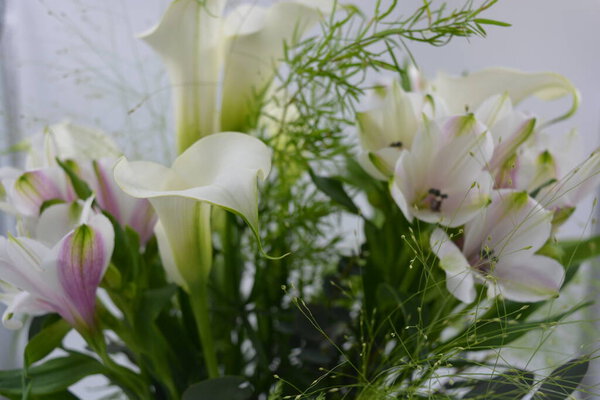 A beautiful, festive and bright bouquet, a composition of white calla lilies, purple white orchids, flowers with green leaves, branches.