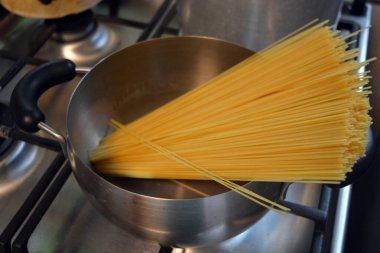 Güzel ve sağlıklı yiyecekler, yemek. Uzun İtalyan siyah buğdaylı vermicelli gri metal bir tencerede sıcak suyla kaynatılır..