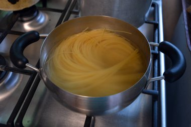 Güzel ve sağlıklı yiyecekler, yemek. Uzun İtalyan siyah buğdaylı vermicelli gri metal bir tencerede sıcak suyla kaynatılır..