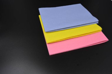 Temizlik malzemeleri, yeni sentetik pembe, sarı, mavi paçavralar, temiz peçeteler siyah plastik arka planda yer alıyor..