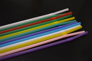 Alışılmadık geçmişleri, sanat eserleri. Birçok kırmızı, beyaz, mavi, yeşil, mor, pembe, sarı plastik pipetler siyah parlak arka planda yer almaktadır..