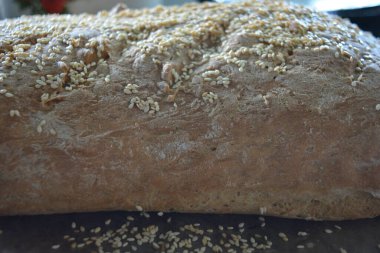 Food, homemade white bread with sesame seeds is located on a black metal baking sheet. Fluffy loaf, bread rolls made at home. clipart