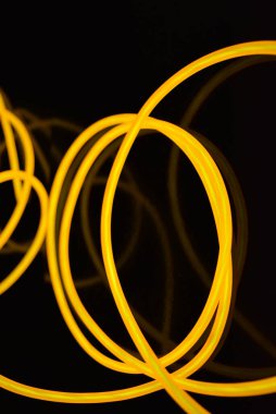 Güzel, kalın, turuncu kablolar kaotik bir şekilde siyah plastik bir arka planda yer alıyor ve bükülüyor. Elektroaydınlatma kablosu, neon tüpleri, plastiğin içindeki ışık, kablolar, ışıklandırma, yaratıcılık.