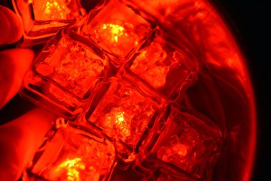 Güzel ve parlak kırmızı parlayan buz küpleri temiz suyla paslanmaz çelik bir kepçenin içinde yüzerler. Buz kübü şeklinde plastik şeyler, su-metal yüzeyini aydınlatmaktadır..