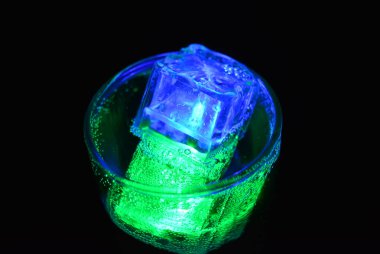 Parlayan buzlu bardakta güzel, parlak bir içki, eğlence için bir parti, bir tatil. Parlak yeşil ve mavi renkli şeffaf küpler bir cam kadehte yer alır..