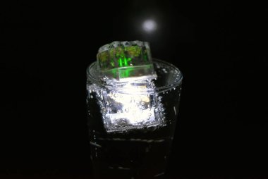 Parlayan buzlu bardakta güzel, parlak bir içki, eğlence için bir parti, bir tatil. Parlak beyaz ve yeşil renkli şeffaf küpler bir cam kadehte yer alır..