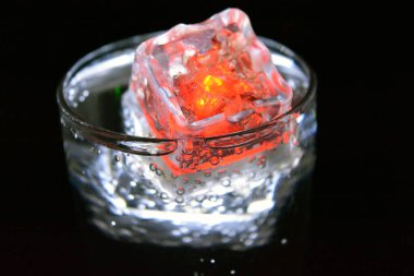 Parlayan buzlu bardakta güzel, parlak bir içki, eğlence için bir parti, bir tatil. Parlak beyaz ve kırmızı renkli şeffaf küpler bir cam kadehte yer alır..