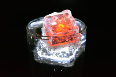 Parlayan buzlu bardakta güzel, parlak bir içki, eğlence için bir parti, bir tatil. Parlak beyaz ve kırmızı renkli şeffaf küpler bir cam kadehte yer alır..