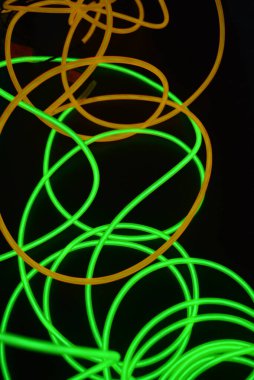 Parlak parlak kablolar, yeşil, limon, kireç, turuncu, turuncu ışık çizgileri. Neon kaotik çizgiler spiraller, daireler ve kıvrımlar halinde siyah bir arkaplanda dizilir..