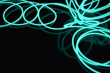 Parlak parlak elektroaydınlatma kabloları, açık yeşil, yeşil, mavi, gök mavisi, turkuaz kalın ışık çizgileri. Neon kaotik çizgiler spiraller, daireler ve kıvrımlar halinde siyah bir arkaplanda dizilir..