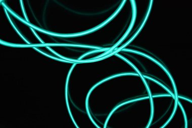 Parlak parlak elektroaydınlatma kabloları, açık yeşil, yeşil, mavi, gök mavisi, turkuaz kalın ışık çizgileri. Neon kaotik çizgiler spiraller, daireler ve kıvrımlar halinde siyah bir arkaplanda dizilir..